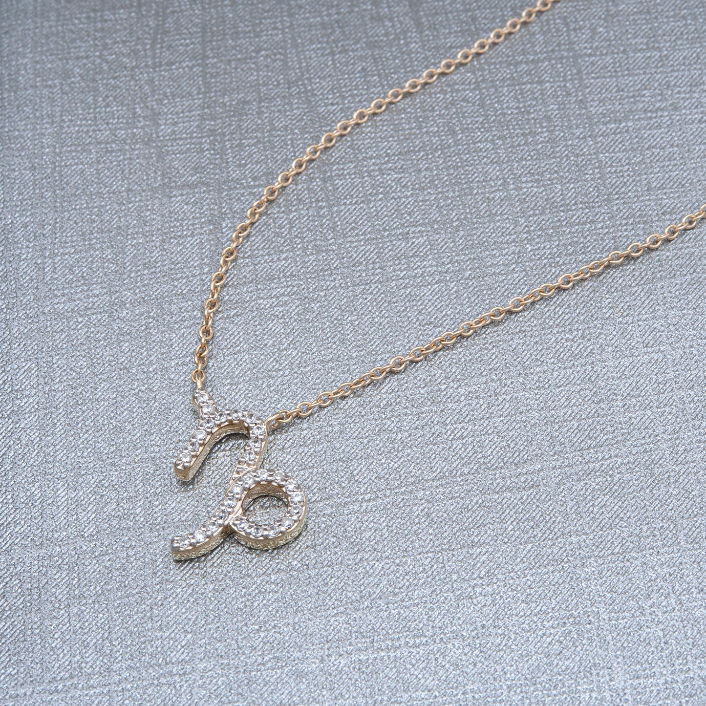 Capricorn Zodiac Diamond Necklace with Gold Chain Placed on cloth